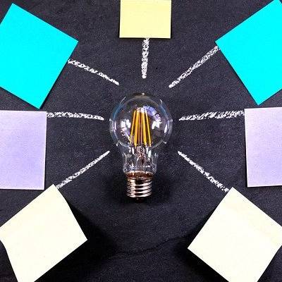 Lightbulb surrounded by colorful sticky notes arranged in a radial pattern, symbolizing inclusive brainstorming and neurodiverse idea generation